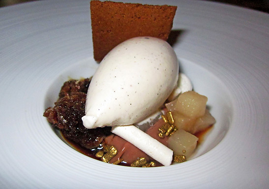 pear marinated in cognac, encrusted with a white meringue coating and encircled by chocolate nuggets and vanilla ice cream