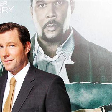 Edward Burns behind a poster of the Alex Cross movie featuring Tyler Perry