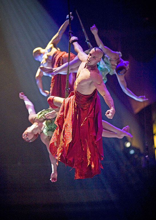 acrobats supported on a cable performing aerial gymnastics high above the pool