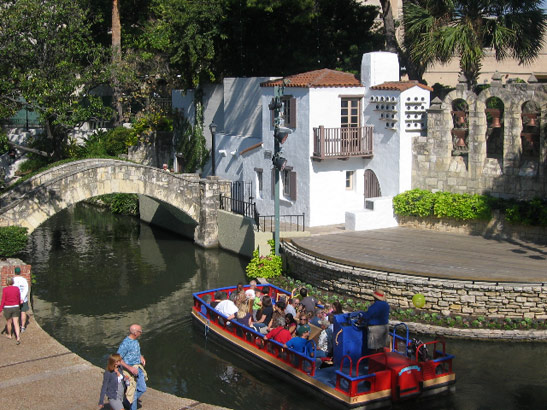 a boat filled with visitors glides along the River Walk, San Antonio