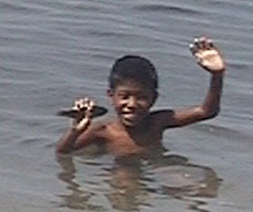 a boy at a wharf in Camiguin waving for boat passengers to throw coins