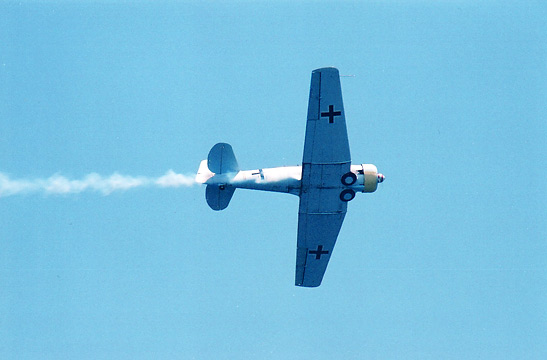 plane with German WW2 markings trailing smoke passes over the SS Lane Victory at a convoy battle recreation