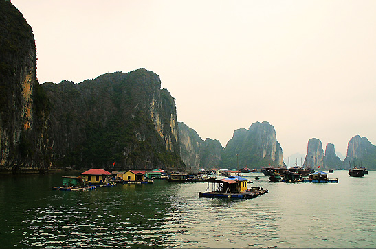 houses on rafts with limestone karst formations in the background, Ha Long Bay