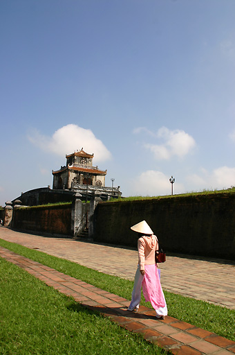 Vietnamese woman in traditional dress walking just outside the Hue citadel wall
