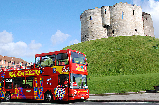 red tourist bus stopping in front of York Castle perched on its artificial mound, York, England
