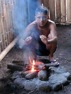 Quichua youth returning from a river swim warming himself by a fire