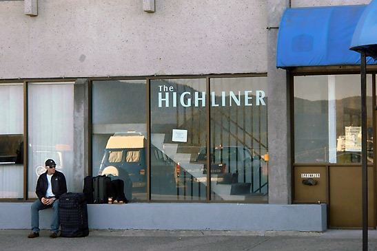 passenger sitting on a sidewalk outside a buss office, Highliner Inn, Prince Rupert