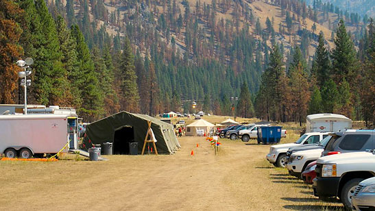 helicopter departing from fire camp ; green dining tent near the middle of the picture