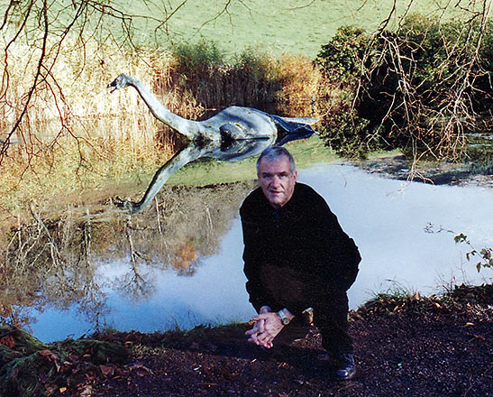 author poses near a pond and a replica of Nessie, Loch Ness