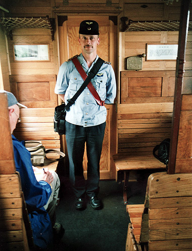 train conductor standing amidst wooden seats inside steam train